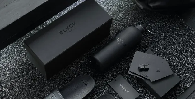 Black presentation boxes, a bottle and small leather goods laid out on a dark surface.
