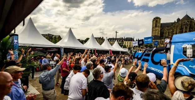 A crowd with arms raised beside white hospitality marquees, a cathedral tower behind them.